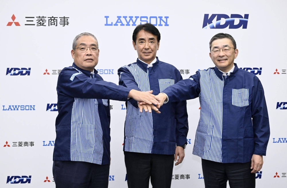 Mitsubishi President Katsuya Nakanishi (left), Lawson President Sadanobu Takemasu (center) and KDDI President Makoto Takahashi wear Lawson uniforms during a news conference in Tokyo on Tuesday to announce the carrier's plan to raise its stake in the convenience chain.