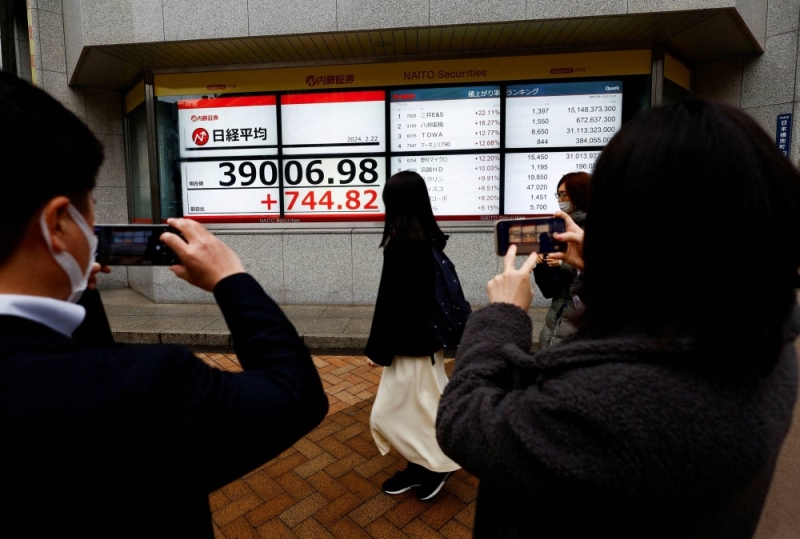 People take photos of electronic screens showing the Nikkei average surging to its highest level ever, outside a brokerage in Tokyo on Thursday.
