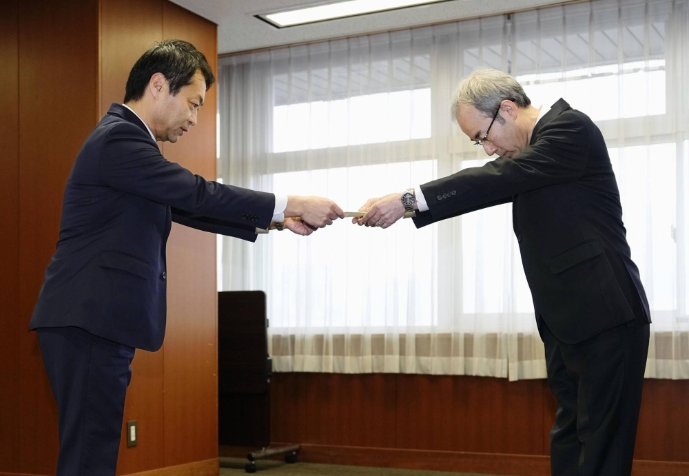 Toyota Industries President Koichi Ito (right) receives an operation correction order from transport ministry director-general Hirohisa Tsuruta at the transport ministry in Tokyo on Thursday.