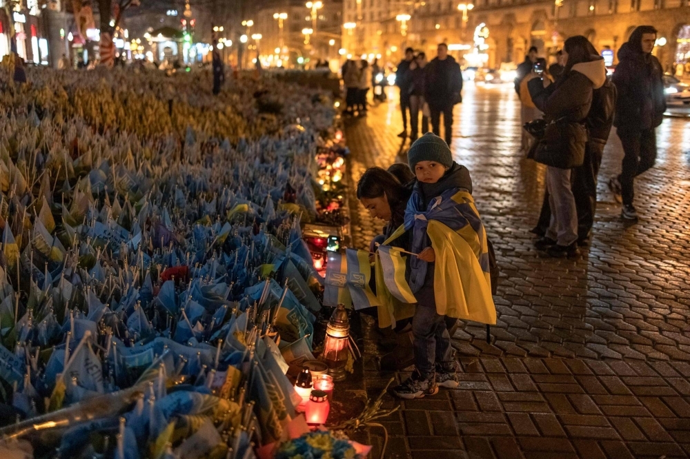 A woman and children place flags for friends who are in the Ukrainian military at Independence Square in Kyiv on Saturday. 