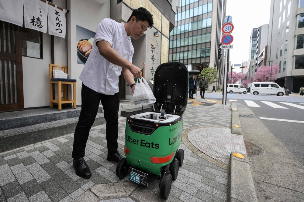 A restaurant employee places a food order into the storage compartment of Uber Eats' self-driving robot during a demonstration of the service on Tuesday.