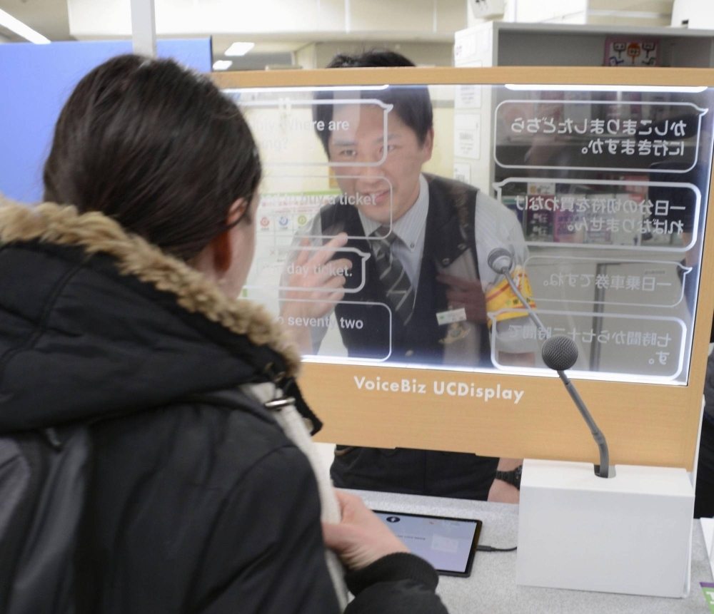 A woman uses a transparent translation screen covering 12 languages as a station employee looks on at the Oedo Line's Tochomae Station in Tokyo's Shinjuku Ward on Feb. 29.