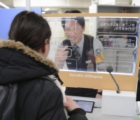 A woman uses a transparent translation screen covering 12 languages as a station employee looks on at the Oedo Line's Tochomae Station in Tokyo's Shinjuku Ward on Feb. 29. | KYODO