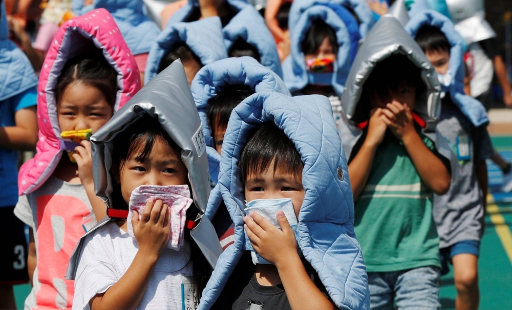 Schoolchildren wearing padded hoods to protect themselves from falling debris take part in an earthquake simulation drill at an elementary school in Tokyo in August 2018.