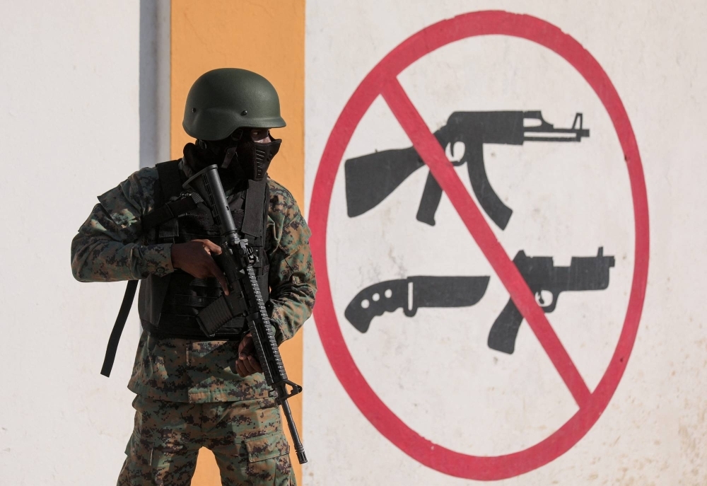An armed soldier stands guard next to a sign prohibiting the use of weapons outside the military headquarters as Haiti continues in a state of emergency, in Port-au-Prince, Haiti, on March 6.