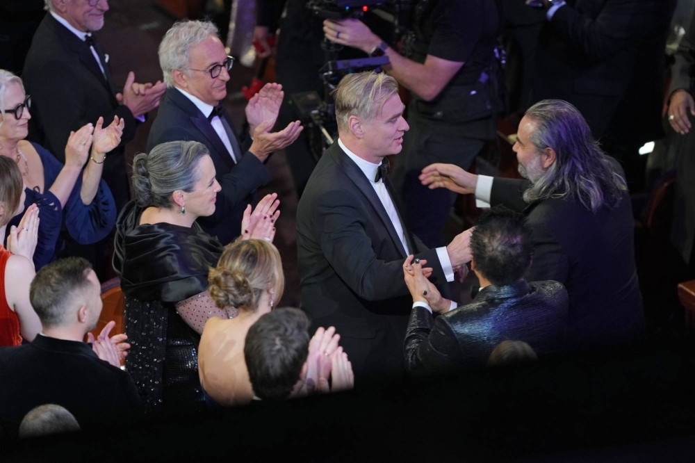 Christopher Nolan (center) embraces Hoyte van Hoytema after he won the award for best cinematography for “Oppenheimer.”