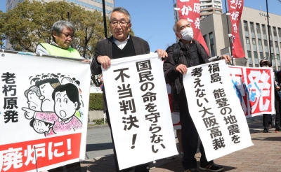 People who sought an injunction to halt the No. 3 unit of Kansai Electric Power's Mihama power plant in Fukui Prefecture hold up signs about the Osaka High Court's ruling in Osaka on Friday.