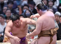 Takerufuji (left) pushes Ryuden over the straw bales on Sunday in Osaka, becoming the first wrestler to secure a winning record by improving to 8-0 at the Spring Grand Sumo Tournament. | Kyodo