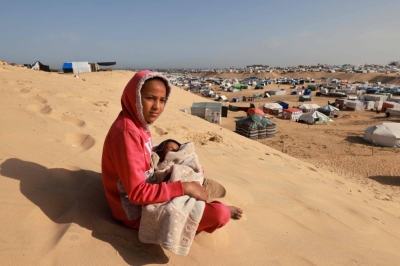 A Palestinian girl sits holding a toddler on a sand dune overlooking a camp for displaced people in Rafah in the southern Gaza Strip on Sunday.