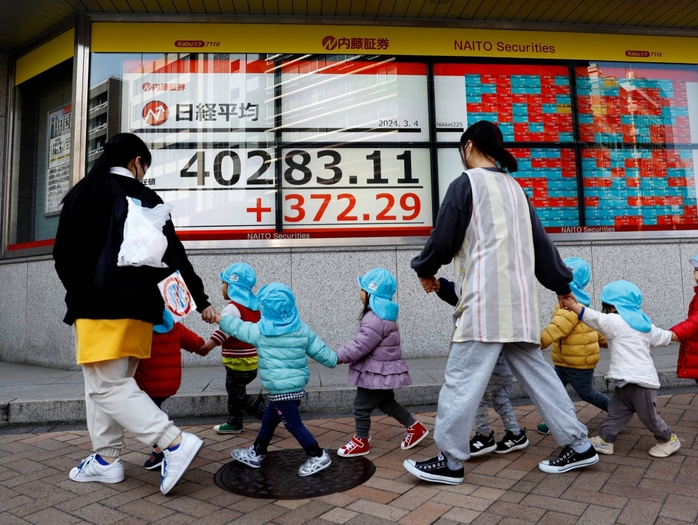 Children and teachers walk past an electronic screen displaying Japan's Nikkei share average outside a brokerage in Tokyo on March 4.