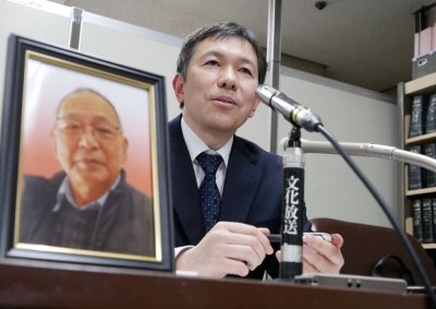 Shizuo Aishima's son speaks to reporters next to a photo of his father in Tokyo on Thursday.