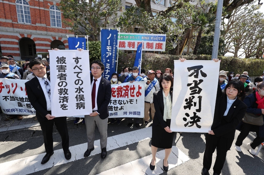 Lawyers representing plaintiffs in lawsuits seeking damages for Minamata disease hold banners outside the Kumamoto District Court in the city of Kumamoto on Friday, criticizing the ruling as “unjust.”