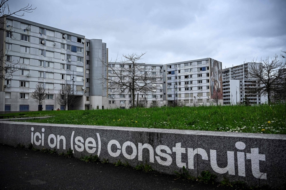 A view of apartment buildings with writing on a wall that reads "Here we build (ourselves)," in the Franc-Moisin neighborhood of Saint-Denis, a northern Paris suburb, on March 13. The Seine-Saint-Denis department north of Paris will host a number of events for the Paris 2024 Olympic and Paralympic Games, with venues including the Stade de France and Aquatics Centre, as well as the Olympic Village.