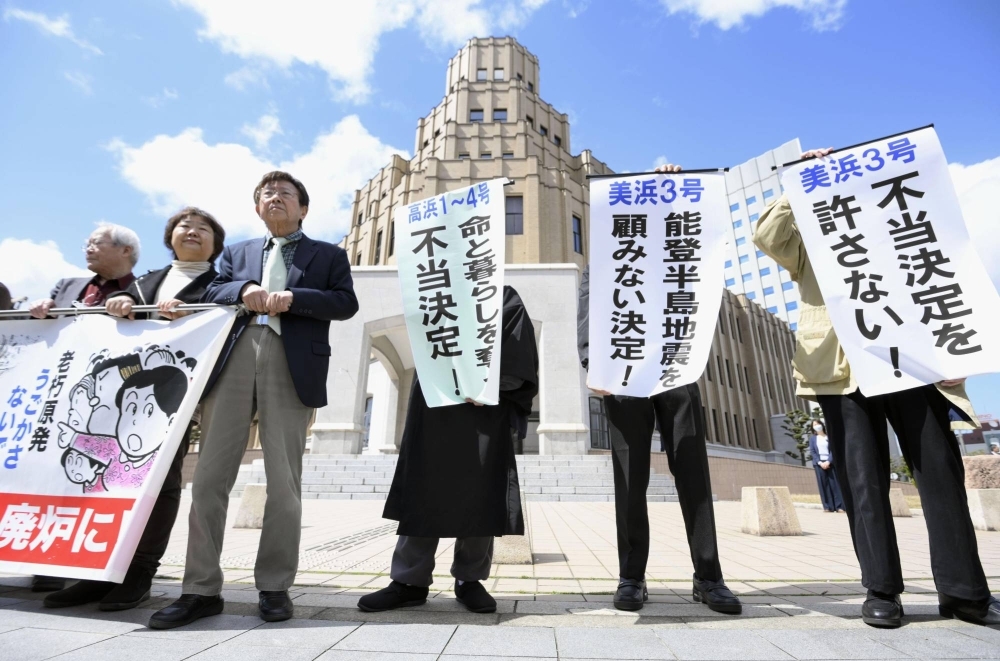 Residents of Fukui Prefecture who filed petitions to suspend aging nuclear reactors at two Kansai Electric Power plants in the prefecture hold up signs in front of the Fukui District Court in Fukui on Friday, criticizing the court's decision to reject the decisions as "unjust."