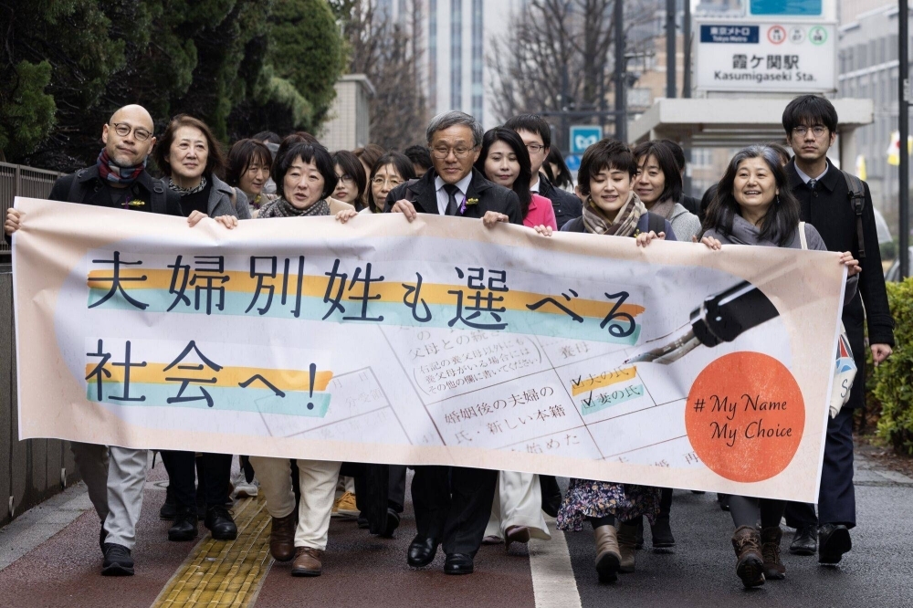 Plaintiffs in a suit against the government over a law that requires married spouses to have the same surname arrive at the Tokyo District Court in Tokyo on March 8.