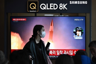 A woman walks past a TV showing a news broadcast with file footage of a North Korean missile test, at the main railway station in Seoul on March 18.