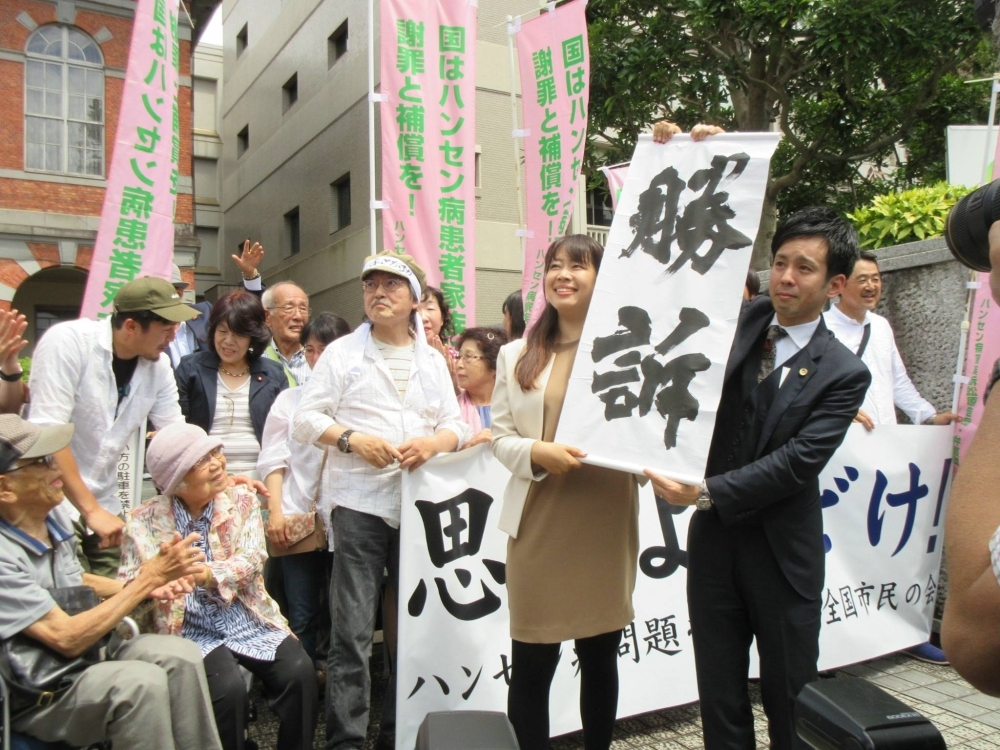 Lawyers representing families of former leprosy patients seeking damages from the state hold up signs in front of the Kumamoto District Court in June 2019 after winning the case.