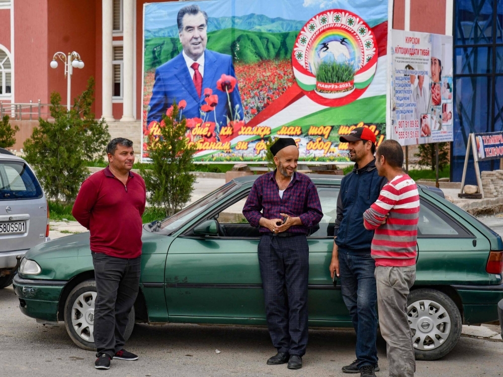 Men stand chatting in front of an image of the Tajik President Emomali Rahmon, in the village of Khuroson, near Obikiik, some 70 kilometers south of the Tajikistan capital Dushanbe, on March 26.