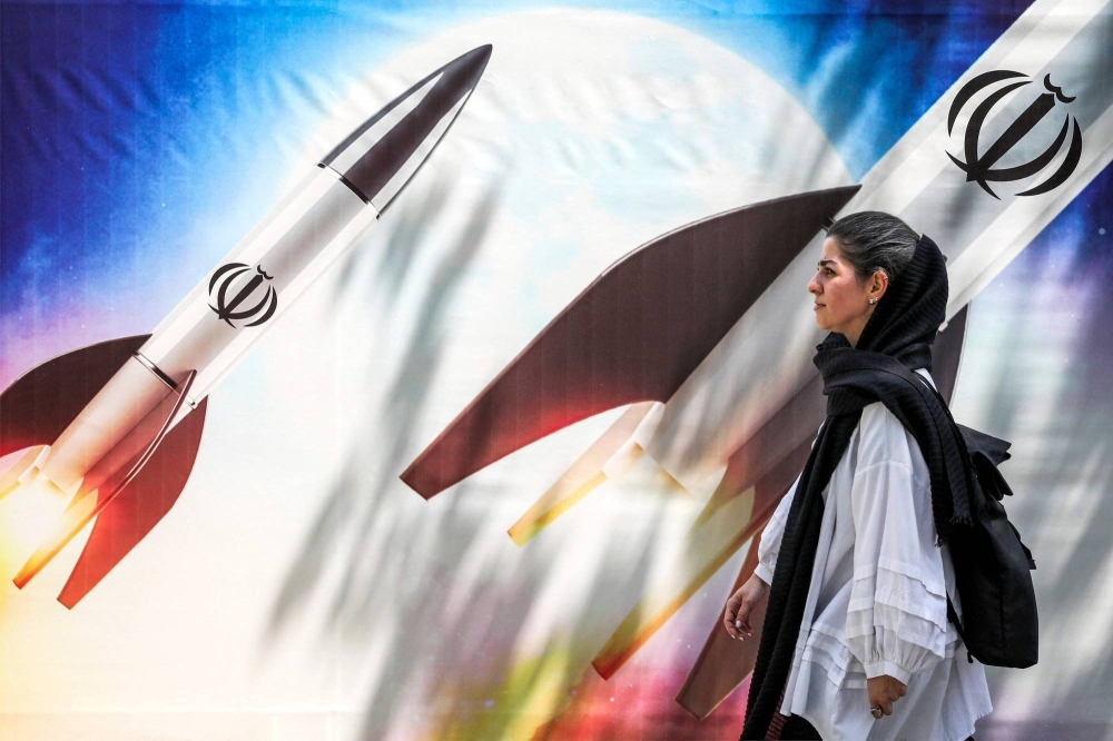 A woman walks past a banner depicting missiles bearing the emblem of the Islamic Republic of Iran being launched, in central Tehran on Monday.