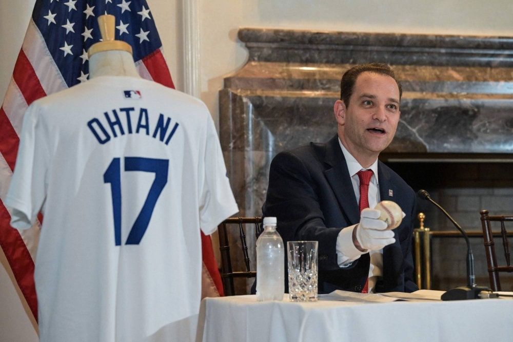Josh Rawitch, president of the National Baseball Hall of Fame, holds a baseball thrown by former Dodgers pitcher Hideo Nomo during a no-hitter in 1996 while seated next to a Dodgers uniform used by Shohei Ohtani this season during a news conference at the U.S. ambassador's residence in Tokyo