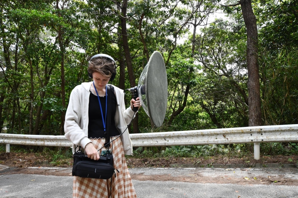 Cassondra George, a research assistant in the Environmental Science and Informatics Section at the Okinawa Institute of Science and Technology, listens to a recording of a bird call captured using a parabolic microphone in Onna, Okinawa Prefecture, on April 4. Parabolic microphones are sometimes used to identify specific bird calls.
