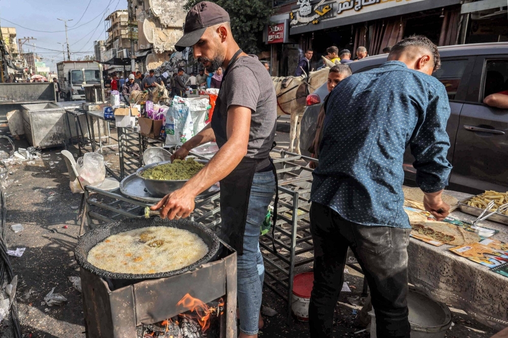 A restaurant worker fries falafel balls as another prepares a flatbread sandwich along a market street in Rafah in the southern Gaza Strip on Tuesday.