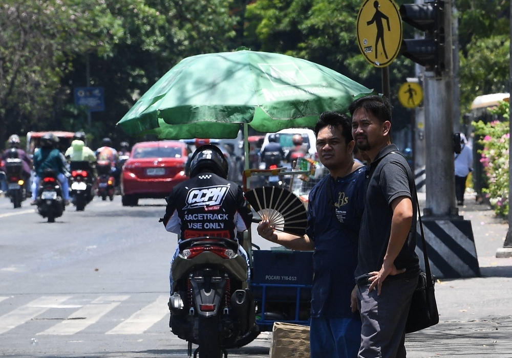 A pedestrian cools himself with a folding hand fan as he waits for a ride along a road in Manila on Wednesday, as extreme heat hit the Philippines.