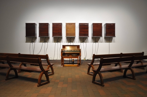 Theaster Gates' “A Heavenly Chord” lines up church pews before seven speakers and a Hammond B3 organ, a type of electric organ prevalent in Black American churches.