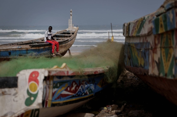Birane Mbaye, one of the survivors of a disastrous attempt to reach Spain last year, sits on a wooden fishing boat at the shore of Fass Boye, Senegal.