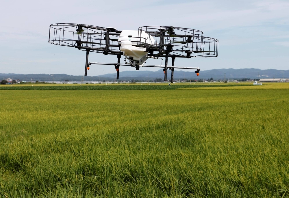 An automated drone flies over rice plants, spraying pesticide while diagnosing growth of individual rice stalks, during a demonstration in Tome, Miyagi Prefecture, in 2018. Although the price of rice monitoring technology might be too steep for family-run farms, the national government provides funds to support such efforts.