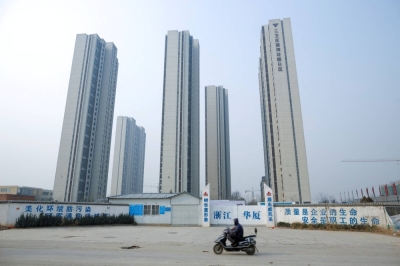 A man rides a scooter past apartment high rises under construction in Zhengzhou, China, in January 2019.