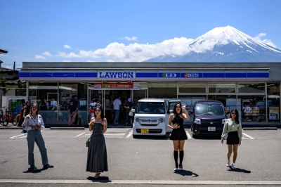 Tourists pose in front of a convenience store with Mount Fuji on Friday in the town of Fujikawaguchiko, Yamanashi Prefecture. Local residents are upset over littering, overcrowding and the inconvenience caused by the visitors.