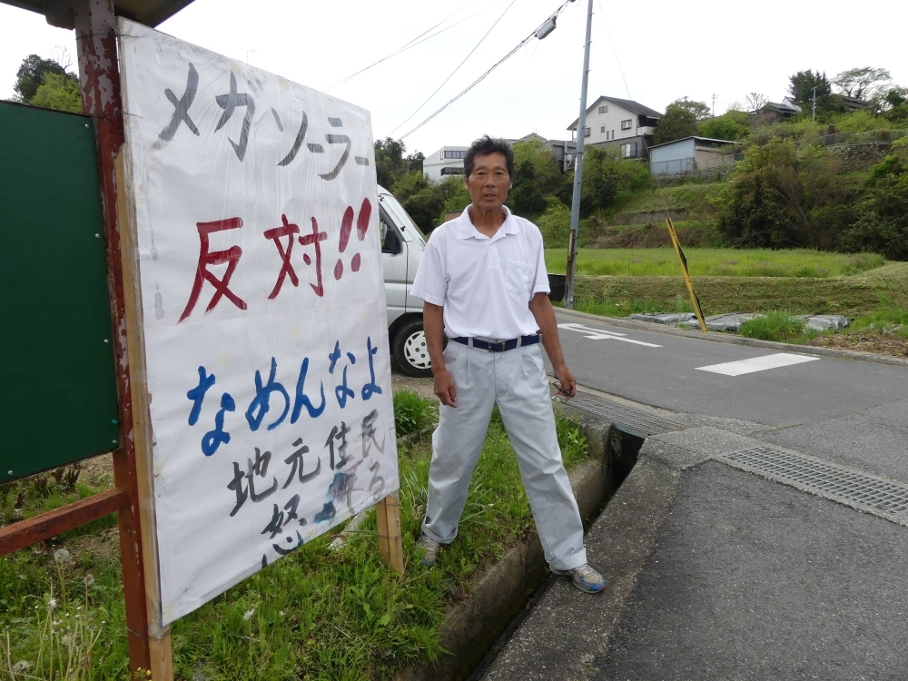 Kozo Ishinage, a resident of the city of Gojo, Nara Prefecture, stands by a handwritten sign expressing opposition to a megasolar farm project in the city proposed by the Nara Prefectural Government. Kozo Ishinage, a resident of the city of Gojo, Nara Prefecture, stands by a handwritten sign expressing opposition to a megasolar farm project in the city proposed by the Nara Prefectural Government.