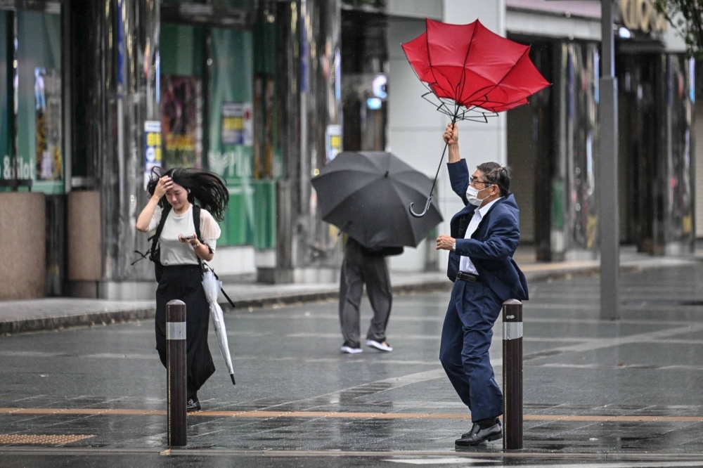 台風19号シャンシャンが鹿児島県に上陸したため、木曜朝、福岡市の博多駅の外では通勤客らが強風と雨と闘った。 台風19号シャンシャンが鹿児島県に上陸したため、木曜朝、福岡市の博多駅の外では通勤客らが強風と雨と闘った。