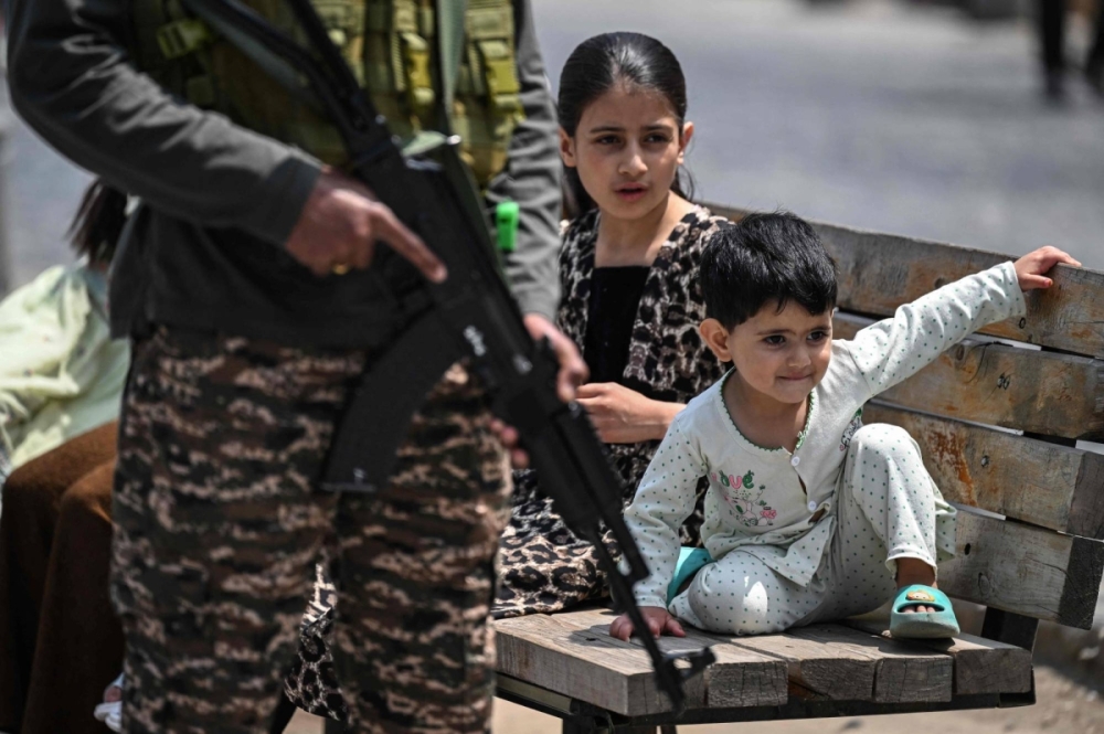 Kashmiri children sit on a bench at a marketplace as an Indian paramilitary soldier keeps guard along a street in Srinagar in Indian-controlled Kashmir on Sunday. Tensions between the nuclear-armed archrivals have soared since India accused Pakistan of backing a shooting that killed 26 civilians on the Indian side of the disputed territory on April 22.
