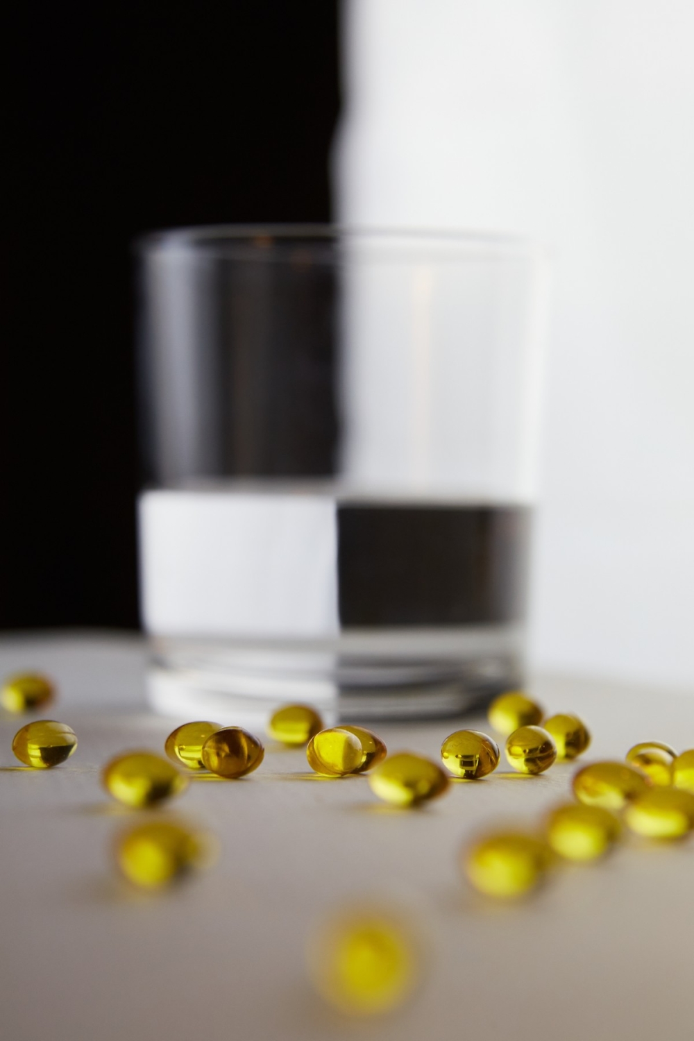 Yellow gelatin capsules and a glass of water on a black and white background. Medical preparations, dietary supplements, vitamins, minerals, probiotics. Taking care of your health. Fat-soluble vitamin Yellow gelatin capsules and a glass of water on a black and white background. Medical preparations, dietary supplements, vitamins, minerals, probiotics. Taking care of your health. Fat-soluble vitamin